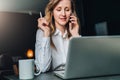 Young businesswoman in shirt is sitting in office at table in front of computer, talking on cell phone Royalty Free Stock Photo