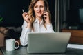 Young businesswoman in shirt is sitting in office at table in front of computer, talking on cell phone Royalty Free Stock Photo
