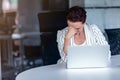 A young businesswoman sits behind her laptop computer frowning with her head in her hands because of a problem at work