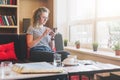 Young businesswoman sits on sofa near window,uses smartphone. Girl chatting, blogging, checking email, working. Royalty Free Stock Photo