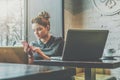 Young businesswoman sitting in cafe at table near window and using smartphone. On desk is laptop and cup of coffee. Royalty Free Stock Photo