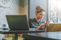 Young businesswoman sitting in cafe at table near window and using smartphone. On desk is laptop and cup of coffee. Royalty Free Stock Photo