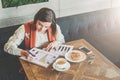 Young businesswoman is sitting in cafe at table, working. Woman is looking at charts, graphs, diagrams.