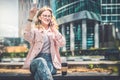 Young businesswoman is sitting on city street and talking on cell phone, raising her hand up. Nearby is cup of coffee. Royalty Free Stock Photo