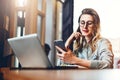 Young businesswoman is sitting in coffee shop at table in front of computer and notebook,using smartphone. Social media.