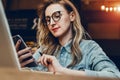 Young businesswoman is sitting in coffee shop at table in front of computer and notebook,using smartphone. Social media. Royalty Free Stock Photo