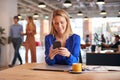 Young Businesswoman Sitting At Desk Using Mobile Phone In Modern Open Plan Office Royalty Free Stock Photo