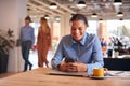 Young Businesswoman Sitting At Desk Using Mobile Phone In Modern Open Plan Office Royalty Free Stock Photo