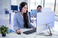 A young businesswoman sitting at her desk, wearing headset and using desktop PC to work in the corporate office. Royalty Free Stock Photo