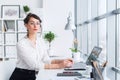 Young businesswoman sitting at her workplace, working out new business ideas, wearing formal suit and glasses, looking