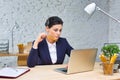 Young businesswoman sitting with laptop at desk against brick wall in office Royalty Free Stock Photo