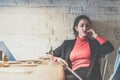 Young businesswoman sitting in restaurant at table, leaning against white brick wall and talking on cell phone. Royalty Free Stock Photo