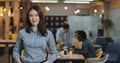 Young businesswoman standing in the modern office, smiling and looking into the camera. Working people on the blurred