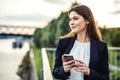 A young businesswoman standing on the river bank, using smartphone. Royalty Free Stock Photo
