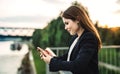 A young businesswoman standing on the river bank, using smartphone. Royalty Free Stock Photo