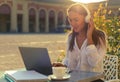 Young businesswoman or student holding headset and looking to her laptop at cafe Royalty Free Stock Photo