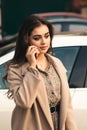 Young businesswoman talking on mobile phone outside. Stylish woman standing by her electro car