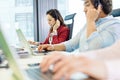 Young businesswoman using headset and laptop with colleagues in foreground at office Royalty Free Stock Photo