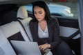 Young businesswoman using laptop while sitting on the back seat of a car, working online. Business, road trip Royalty Free Stock Photo