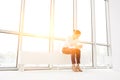 Young businesswoman using smartphone while sitting on radiator at new empty office with yellow lens flare in background