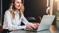 Young businesswoman in white shirt is sitting in office at table in front of computer, typing on laptop. Woman working