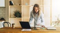 Young businesswoman woman is standing near kitchen table,reading documents,uses laptop,working, studying. Royalty Free Stock Photo