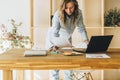 Young businesswoman woman is standing near kitchen table,reading documents,uses laptop,working, studying. Royalty Free Stock Photo