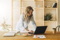 Young businesswoman woman is standing near kitchen table,uses laptop,working, studying.On table tablet computer Royalty Free Stock Photo