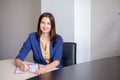 Young businesswoman working at desk in office, taking notes into personal calendar, smiling. Royalty Free Stock Photo