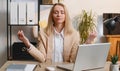 Businesswoman working on laptop meditating doing yoga breathing exercise in lotus position at office Royalty Free Stock Photo