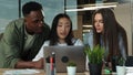 Young businesswoman working on laptop at desk in modern open plan start up office being joined by woman and man Royalty Free Stock Photo