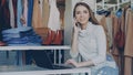 Young businesswoman is working with laptop and talking on mobile phone in her shop. Clothes and customer in background Royalty Free Stock Photo