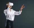 Young businesswoman working in virtual reality environment in VR glasses, presses by her finger on virtual interface on abstract