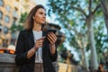 Young businesswoman writes messages on smartphone while walking in a Barcelona Park on Sunny day, female listening to music