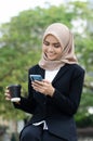 Young businesswomen in black suit and hijab using smartphone and holding cup of coffee Royalty Free Stock Photo