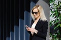 Young businesswomen in black suit using smartphone isolated on background gray wall. Pretty manager holding mobile gadget and Royalty Free Stock Photo