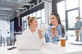 Young businesswomen using laptop and talking at workplace