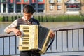 A young busker performing accordion on a riverside street at Sou