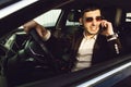 Young bussinesman in suit and black glasses speaks by phone in his car. Bussines look. Test drive of the new car