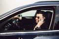 Young bussinesman in suit and black glasses speaks by phone in his car. Bussines look. Test drive of the new car Royalty Free Stock Photo