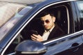 Young bussinesman in suit and black glasses speaks by phone in his car. Bussines look. Test drive of the new car Royalty Free Stock Photo