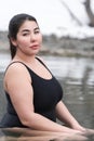 Young busty curvy full figured young model in black swimsuit sitting in outdoors pool at spa resort