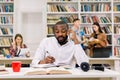 Young busy African man in white shirt, student studying in library at the university, talking on the smartphone and Royalty Free Stock Photo