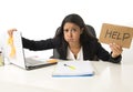 Young busy desperate Latin businesswoman holding help sign sitting at office desk in stress worried