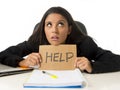 Young busy desperate Latin businesswoman holding help sign sitting at office desk in stress worried