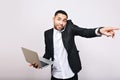 Young busy joyful handsome office worker in white shirt and black jacket holding laptop, talking on phone on white