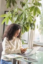 Young busy pretty woman sitting at home holding phone using laptop. Royalty Free Stock Photo