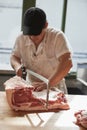 Young butcher sawing meat at a butcher's shop, vertical