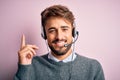 Young call center agent man with beard wearing headset over isolated pink background with a big smile on face, pointing with hand Royalty Free Stock Photo