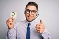 Young call center operator business man with blue eyes holding paper note with question mark happy with big smile doing ok sign, Royalty Free Stock Photo